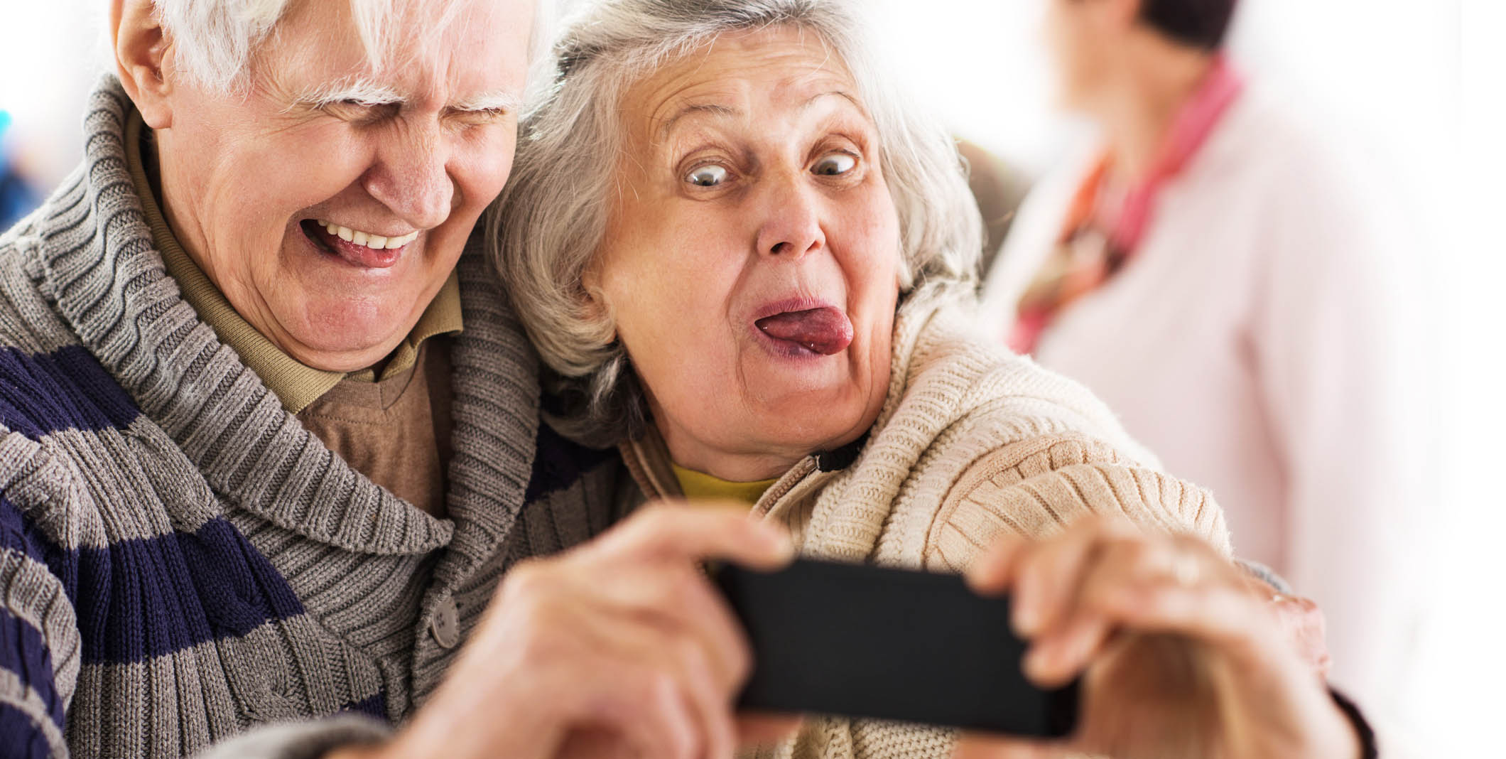 Elderly heterosexual white couple laughing and taking a selfie. The woman has her tongue out.
